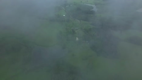 aerial tilt up shot through patches of fog like clouds looking down at the green landscape in latvia