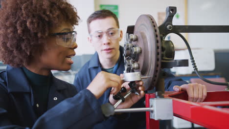 tutor with female students checking car brake discs on auto mechanic course at college