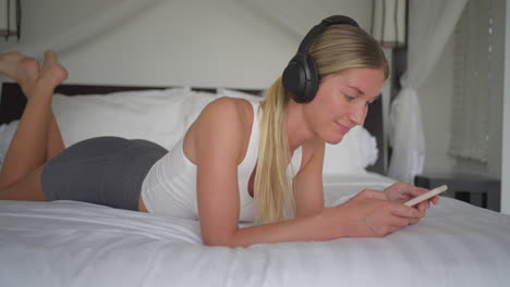 woman listening to music on spotify through smartphone, unwinding in bed concept