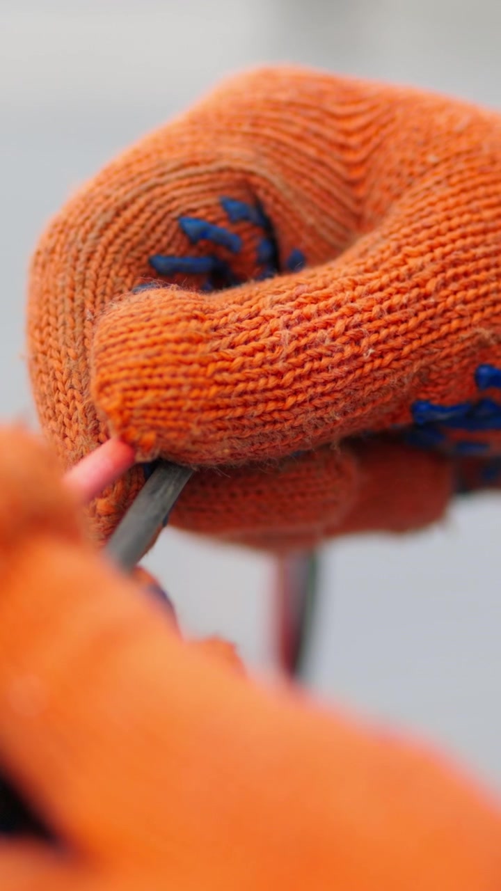 Nærbillede af hænder med orange arbejdshandsker på, der holder en ledning eller et kabel, sandsynligvis under en konstruktion eller