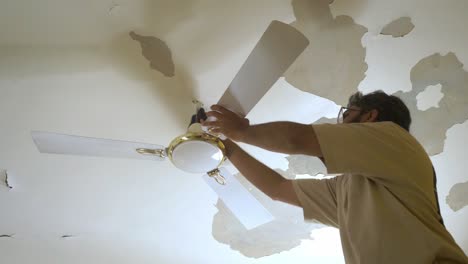 south asian man cleaning ceiling fan of bedroom