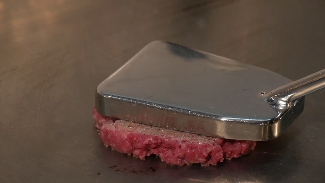 Chef che pressa una palla di carne macinata per formare un hamburger su una piastra calda, vista ravvicinata