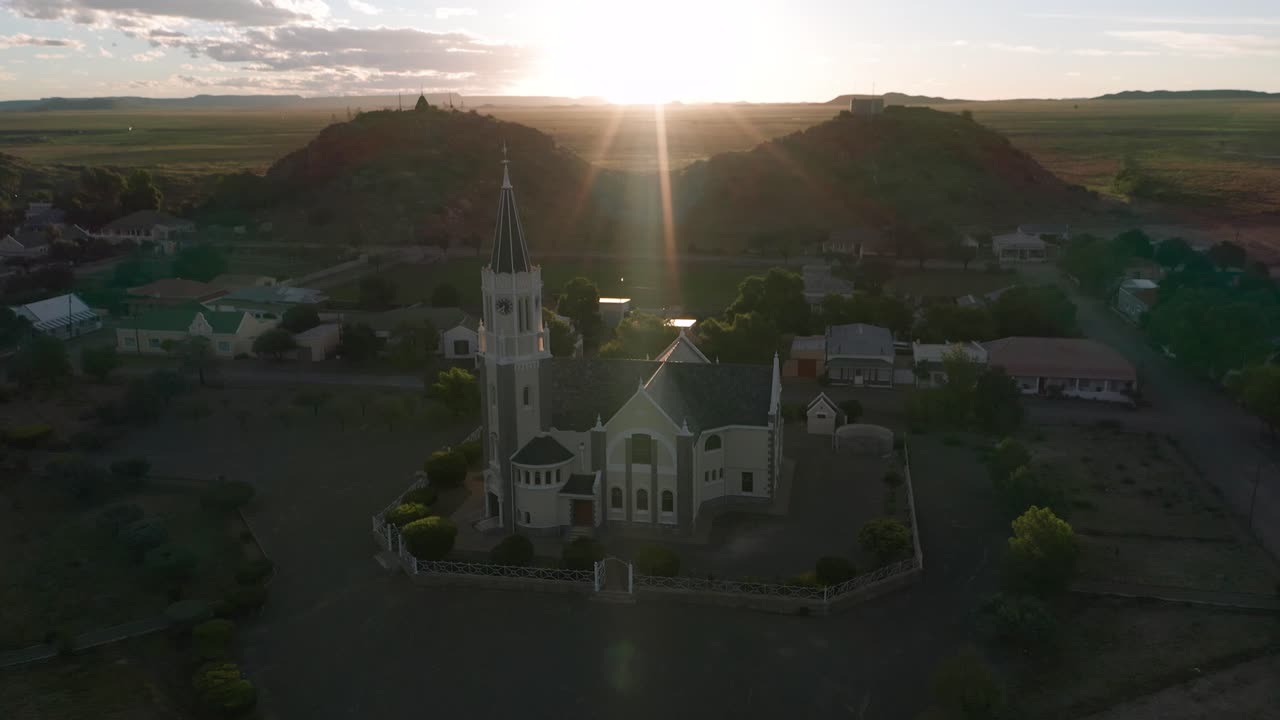 Flying backwards, away from a charming church during sunset, golden hour, aerial
