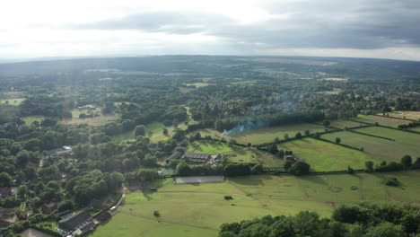 aerial shot of fields and forests in the english countryside, with smoke from a bonfire in the air