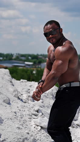 full length view of the attractive handsome muscle man with naked torso looking at his biceps and showing to the camera. american cheerful topless man. vertical video