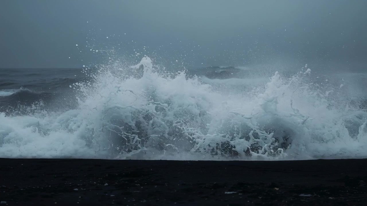 強風によって立ち上がる大きな波が黒い砂浜に打ち寄せ、白い泡と飛沫を飛ばしている。