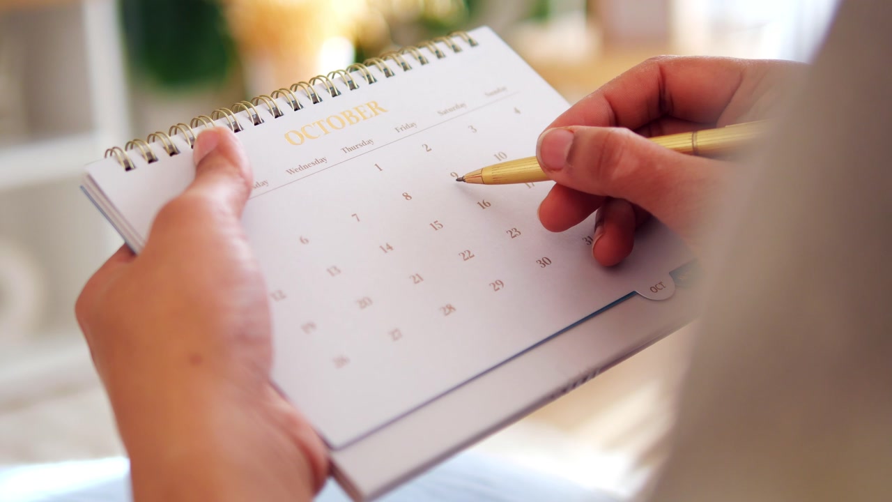 Close-up of Hands Marking Dates on an October Desk Calendar