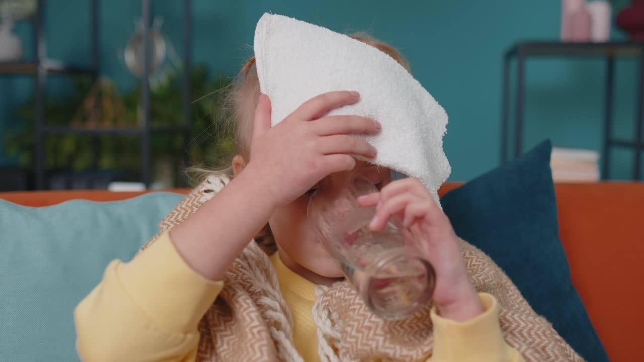 Child girl in plaid suffering from cold or allergy drinking medicine pill tablet water at home room