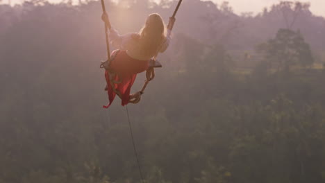 beautiful woman swinging over tropical rainforest at sunrise sitting on swing having fun enjoying freedom on exotic holiday lifestyle slow motion