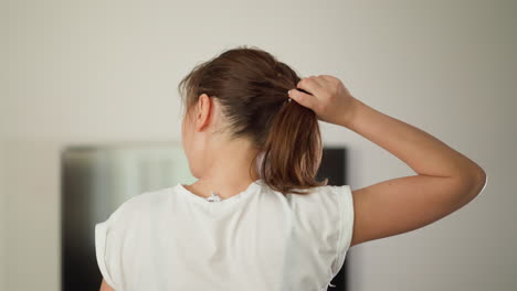 running woman pulls down hair at home. sportive lady in white t-shirt jogs with waving loose hair in domestic gym. exercising for wellbeing