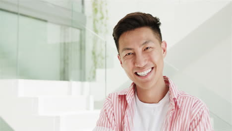 젊은 아시아인 남자가 복사 공간이 있는 현대적인 실내 환경에서 집에서 밝게 미소 짓고 있습니다.