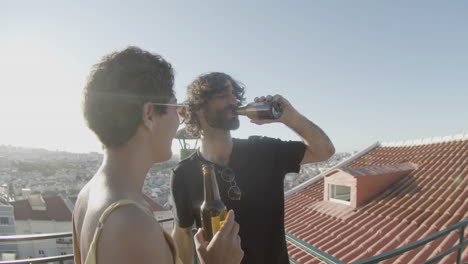 cheerful couple toasting and drinking beer while dancing at rooftop party