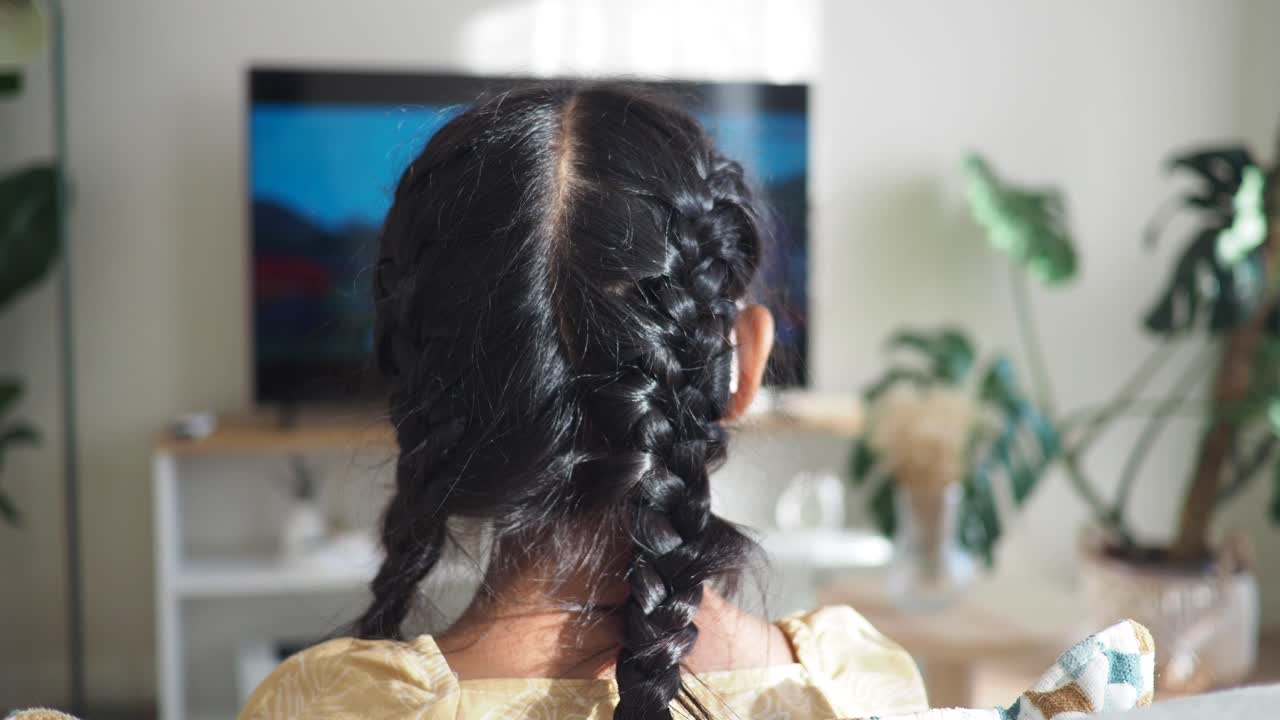 Back view of a person with braided hair watching TV