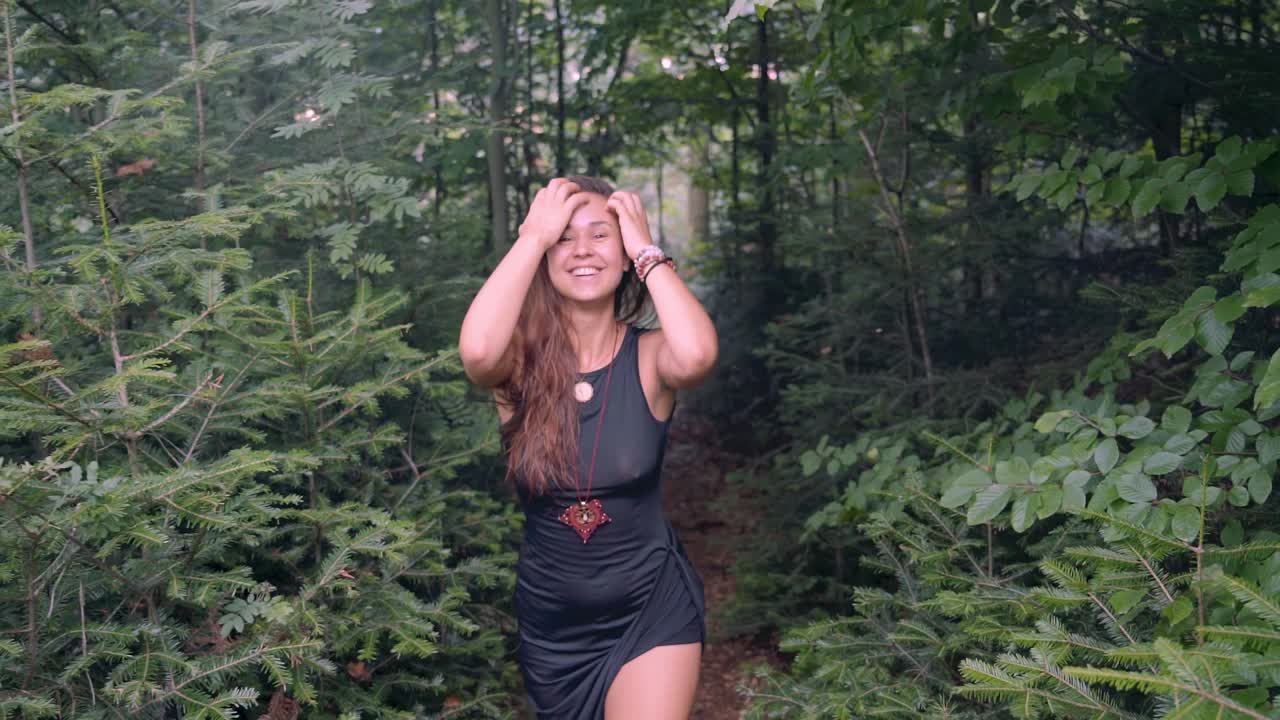 toma de seguimiento en cámara lenta desde el frente de una joven feliz, sexy y hermosa, caminando con una cara sonriente en medio de un denso bosque