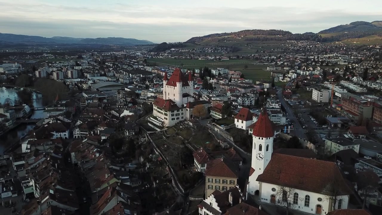 Drohnenaufnahme, die die Stadtansicht von Thun, Schweiz, zeigt, eingebettet entlang der Aare und des Thunersees, mit den majestätischen Schweizer Alpen als atemberaubende Kulisse
