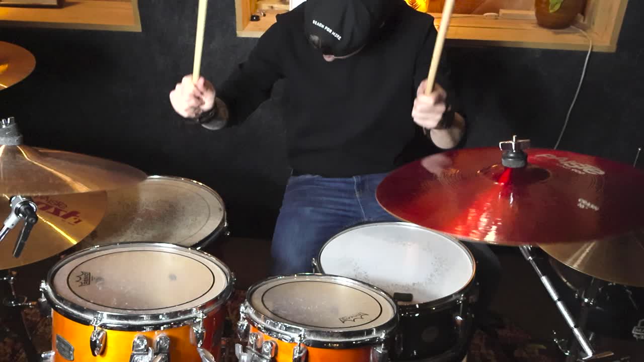 Top down slow motion footage of a man with tattoos playing acoustic reflective and colorful drums or drum set in a studio room. Hitting cymbals, crashes and drumskins hard making the cymbals wobble