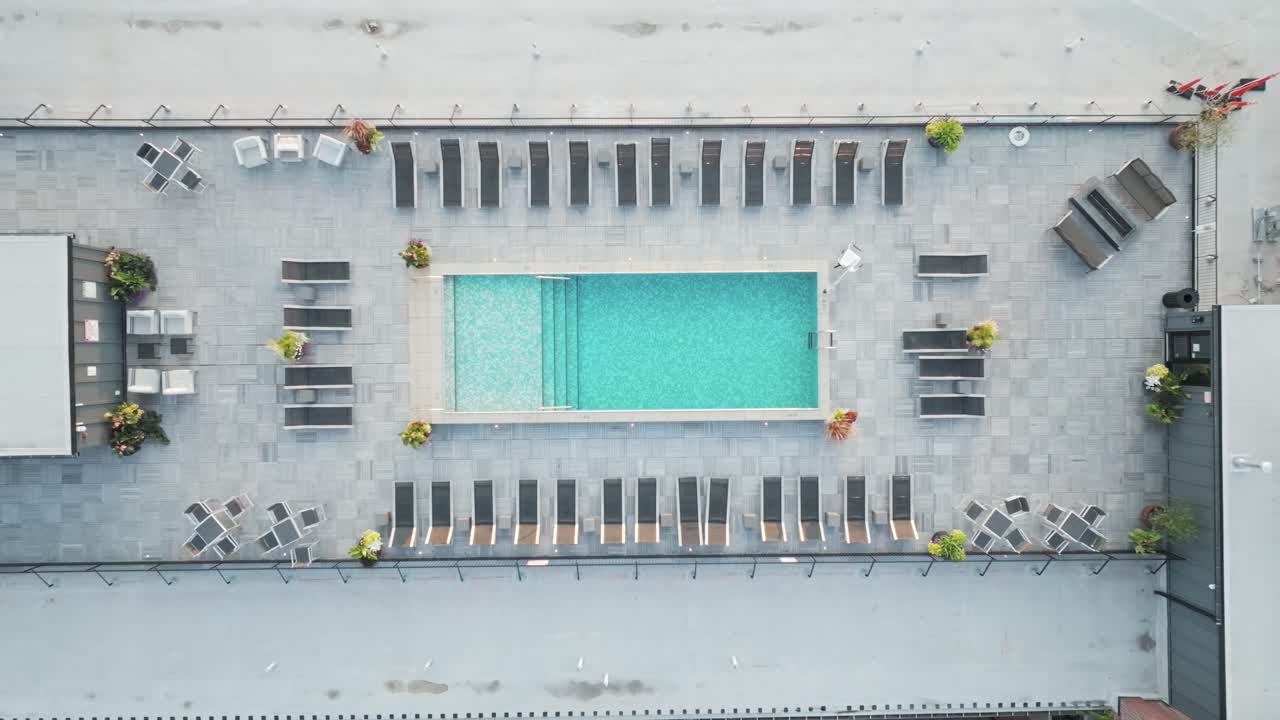 Top-down drone shot of a modern rooftop pool deck surrounded by lounge chairs, located on top of an urban building.