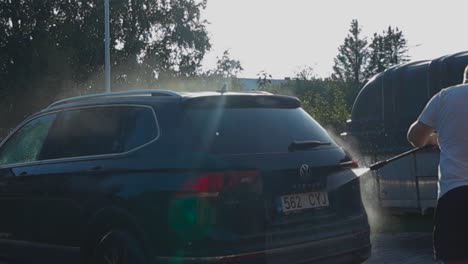 footage captures outdoor car wash using a pressure washer in 4k on summer day. bright sunlight creates beautiful reflections with water while cleaning on a driveway, showing the car's shiny surface.