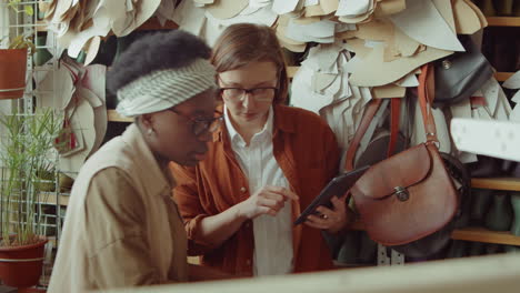 female shoemakers using laptop and discussing shoes in workshop