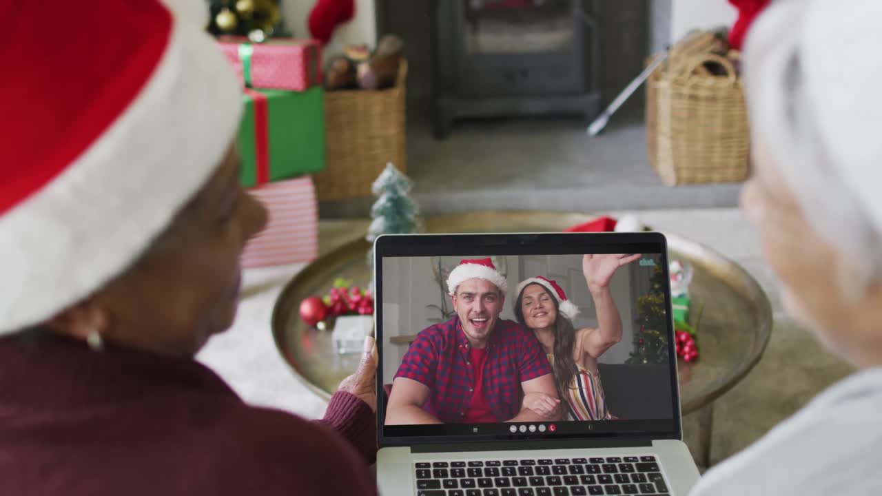 sonriendo diversas amigas mayores usando una computadora portátil para una videollamada de navidad con una pareja en la pantalla