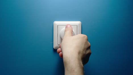 mano masculina gira el botón de atenuante en una pared azul