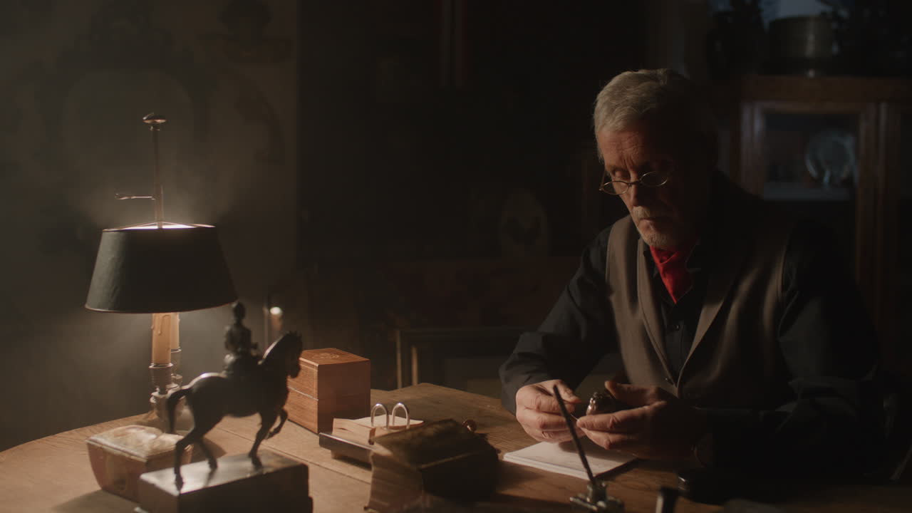 Older passionate man evaluates an old silver skull watch in his office at night