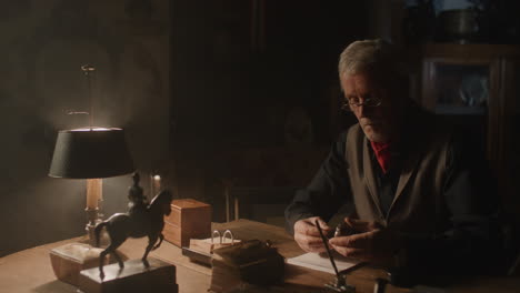 older passionate man evaluates an old silver skull watch in his office at night