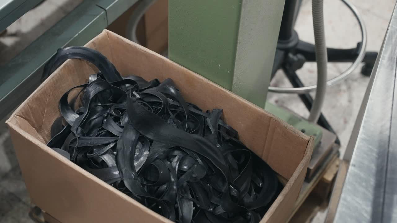 Box containing tangled black rubber strips on workshop floor