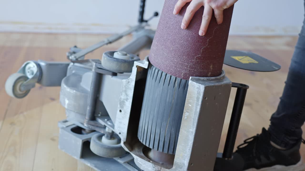 Worker replaces sanding belt into floor sanding machine to prepare for refinishing work