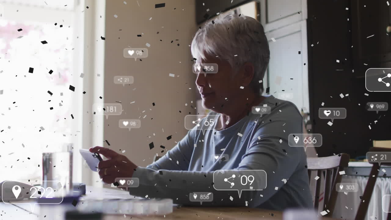 Confetti falling over multiple social media icons floating over senior woman using smartphone
