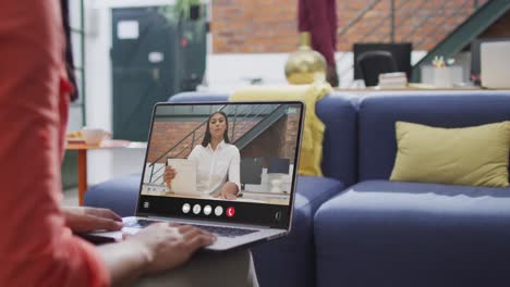 biracial woman using laptop for video call, with business colleague on screen