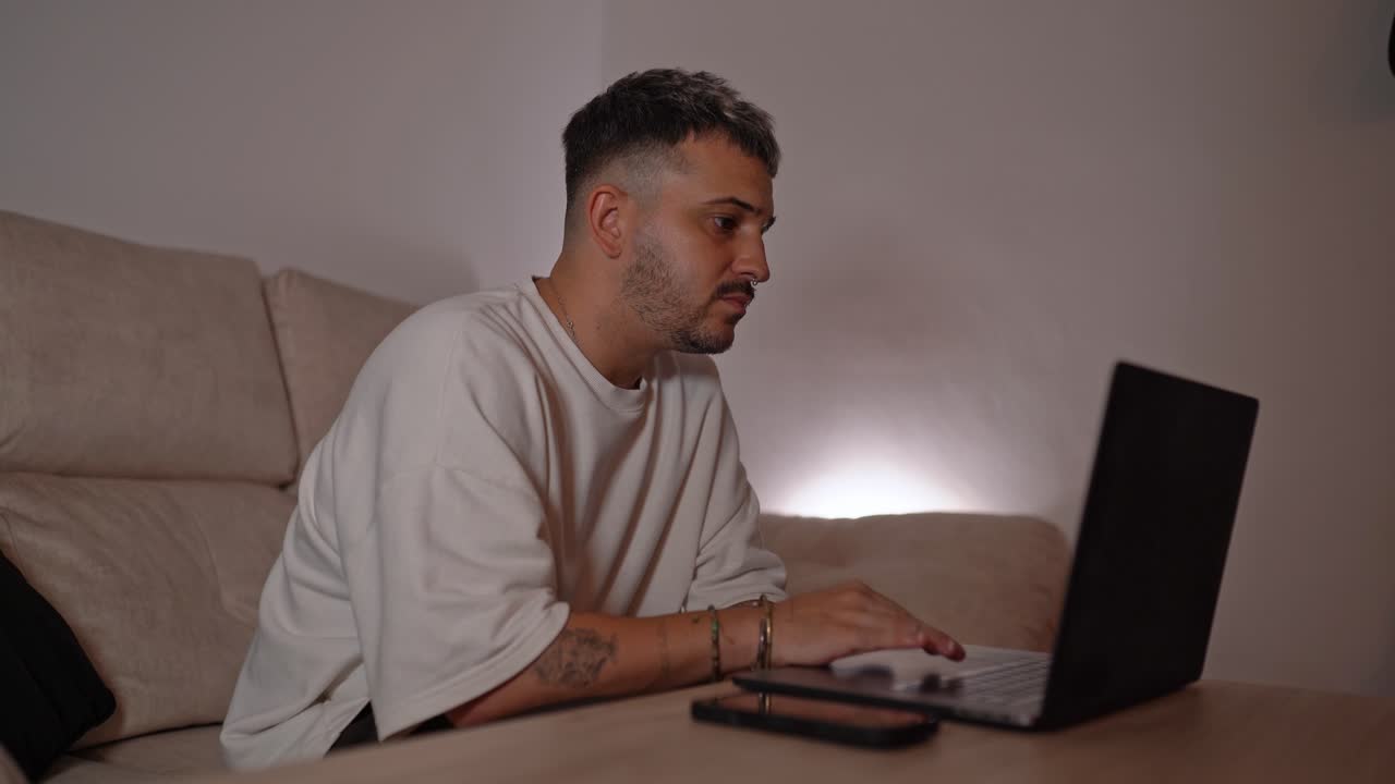 Side view of man using laptop on a table in home setting, appearing focused while browsing or searching for information online