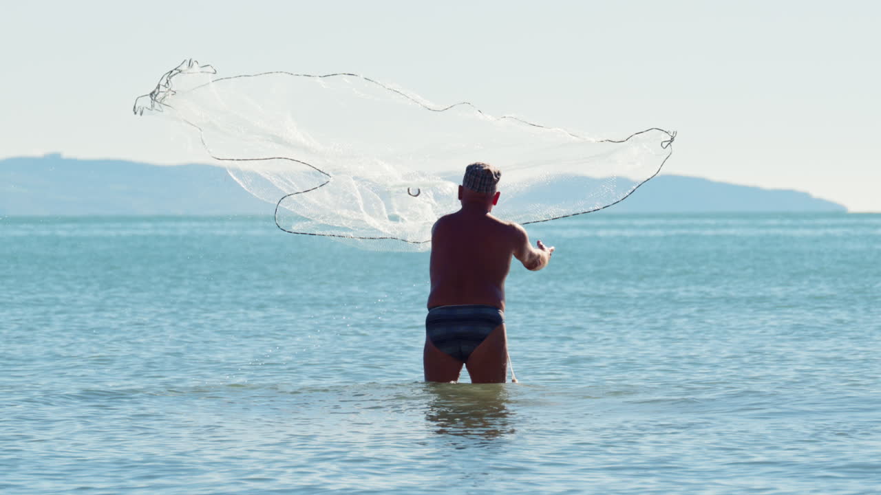 Fisker står i lavt havvand og kaster et traditionelt fiskenet i Albanien