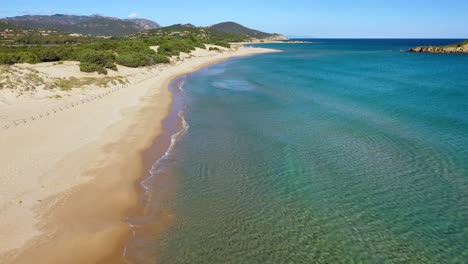 Toma-Aérea-De-La-Hermosa-Playa-De-Su-Giudeu-Sin-Gente,-Agua-Turquesa-Y-Colinas-En-El-Fondo-En-El-Sur-De-Cerdeña,-Italia