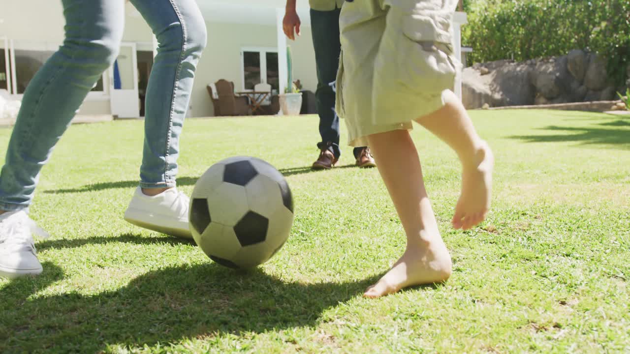 feliz pareja caucásica senior con nieto jugando al fútbol en el jardín