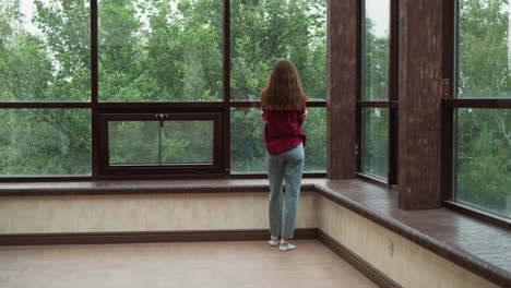 una mujer está de pie junto a una ventana mirando a los árboles.