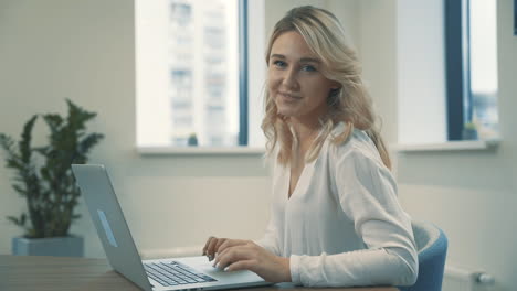 pretty young blonde woman working from home and looking at camera smiling