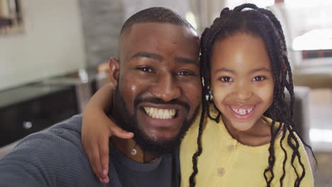 portrait of happy african american daughter and father taking selfie on sofa