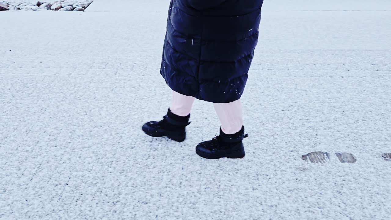 Slow camera glide tracks woman walking left in snowstorm with visible footsteps