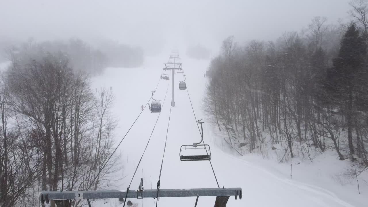 Drone rises above ski lift chairs in snowy weather at resort in Orford, Quebec, Canada