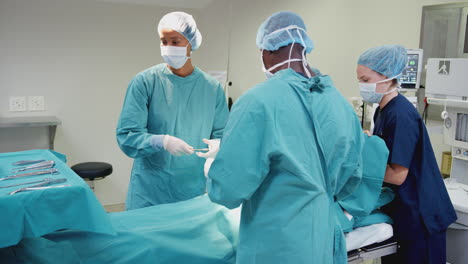 nurse hands surgeon medical instruments as surgical team work on patient in operating theatre