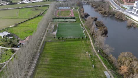 flying over soccer green field and running courts near blue river in spain