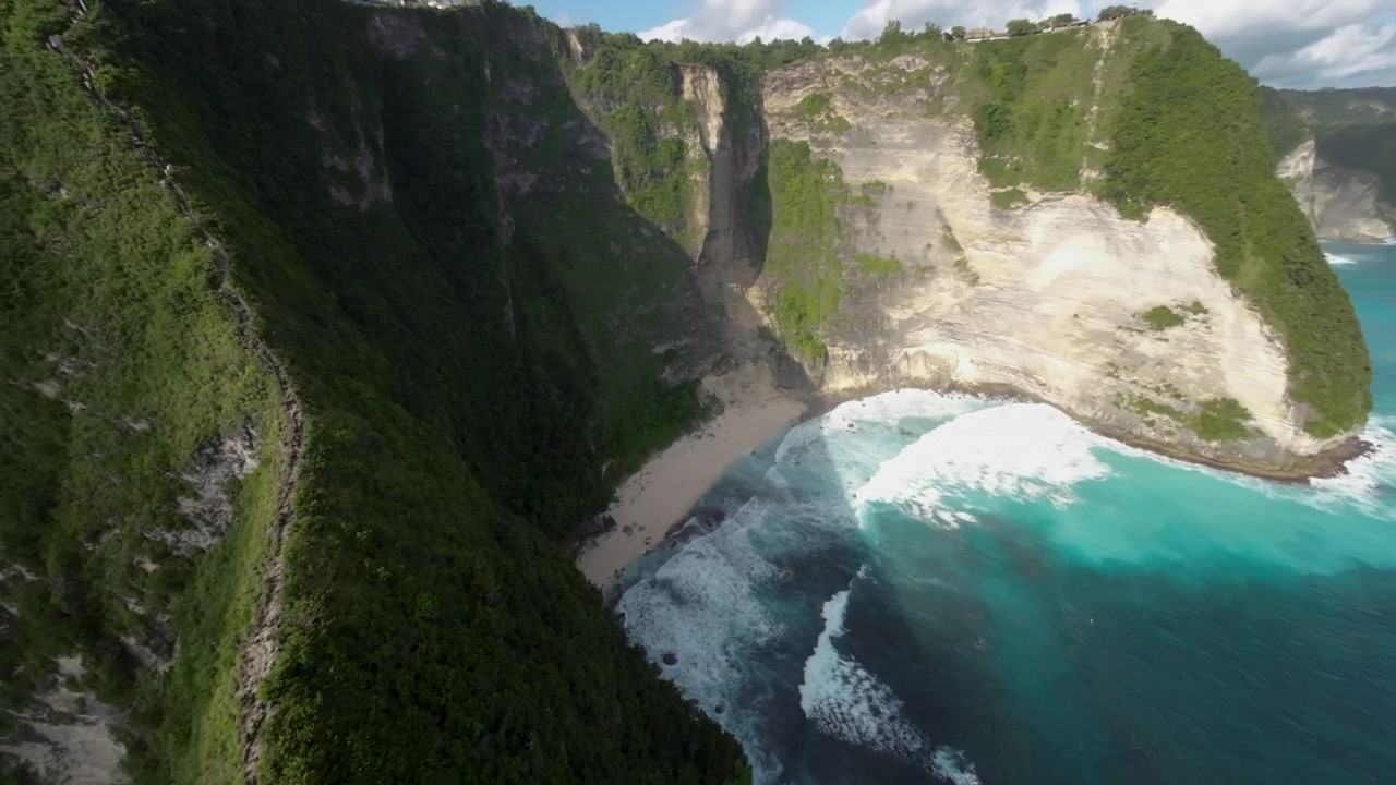 Atemberaubender kinoreifer Drohnenflug, der die dramatischen Kalksteinfelsen, das türkisfarbene Meerwasser und den weißen Sand des Kelingking Beach in Nusa Penida, Bali, zeigt.