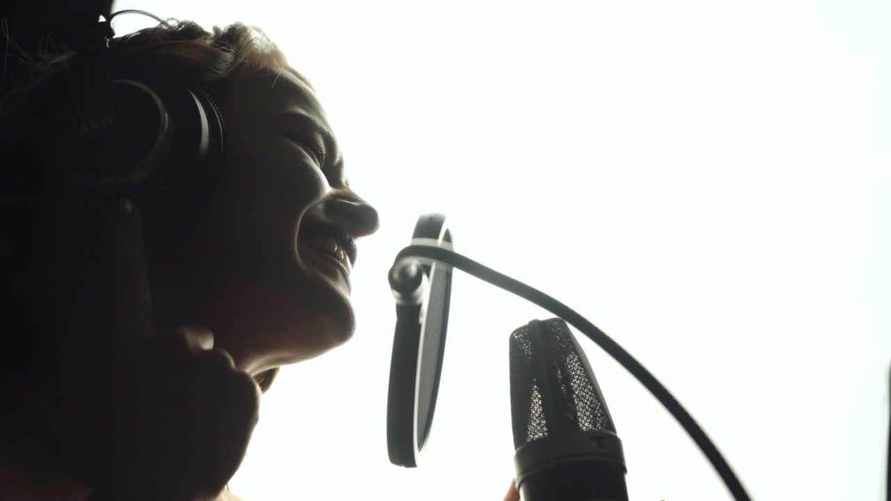 Primo piano di una ragazza con le cuffie che canta una canzone. Studio di registrazione professionale