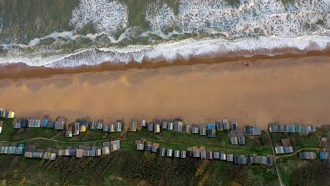 Birds-eye-view-tracking-drone-shot-along-beach-huts-at-Milford-on-Sea-in-UK-during-sunset