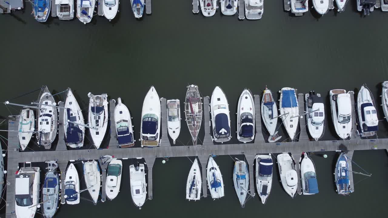 Top down aerial drone view above luxury moored private marina sailing ships and yacht boats dolly left