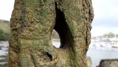 Weathered-eroded-ship-mooring-stone-close-up-view-through-hole-to-sunny-bay-beach