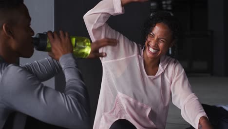 African-american-man-and-woman-resting-after-game-drinking-water-and-laughing