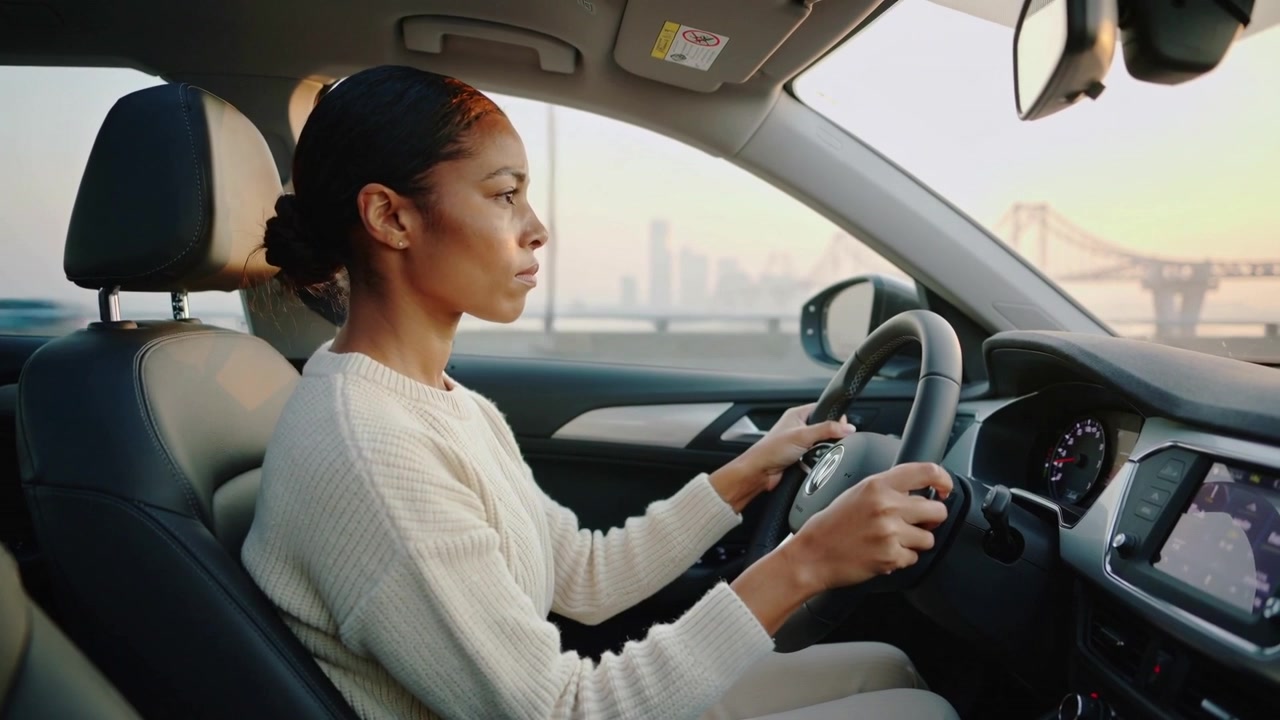 Conducteur afro-américain en pull crème tenant le volant en approchant d'un pont, carte affichée à l'écran.