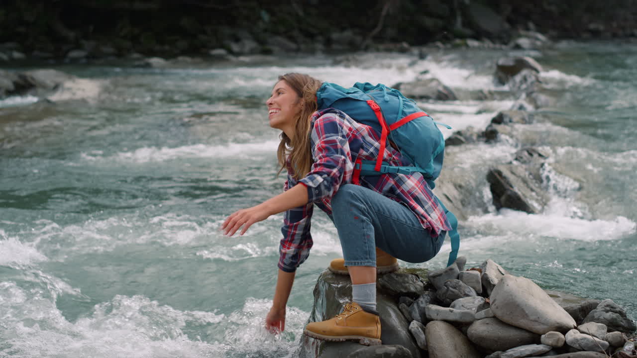 mujer sentada en la orilla del río. excursionista mujer salpicando agua en el aire desde el arroyo
